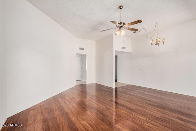 empty room featuring wood-type flooring, lofted ceiling, ceiling fan with notable chandelier, and a textured ceiling