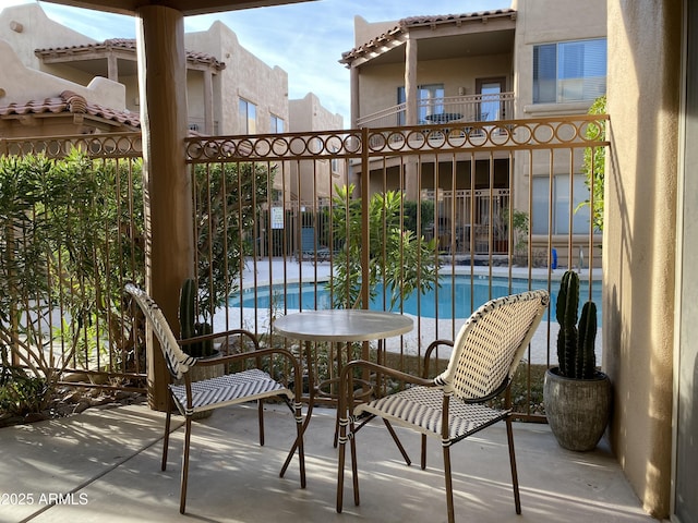 view of patio featuring fence, a balcony, and a community pool