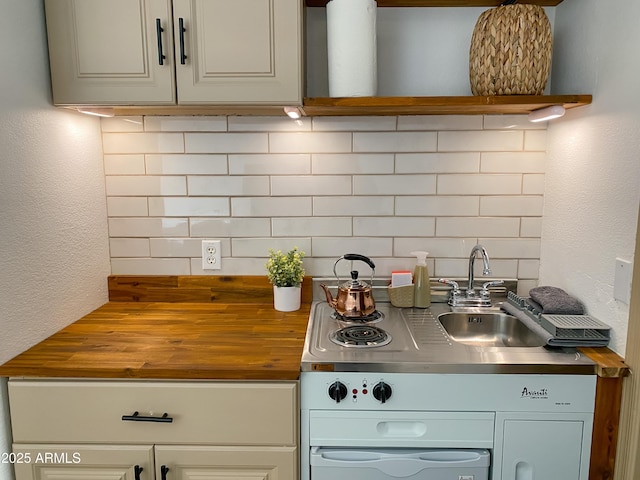 kitchen featuring a textured wall, butcher block counters, a sink, open shelves, and tasteful backsplash