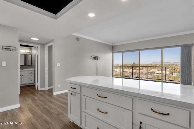 kitchen with a mountain view, white cabinets, crown molding, light hardwood / wood-style flooring, and light stone countertops