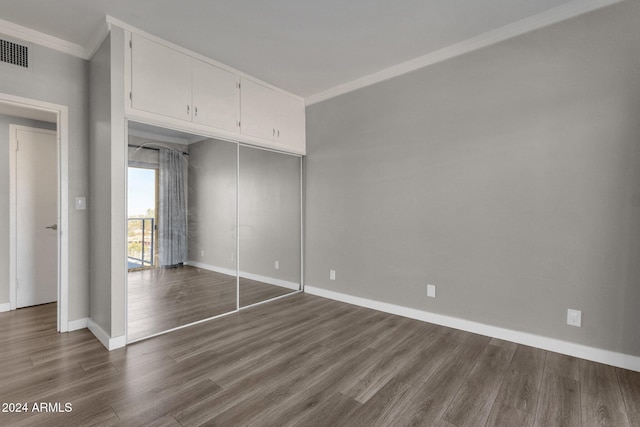 unfurnished bedroom featuring dark hardwood / wood-style flooring, crown molding, and a closet