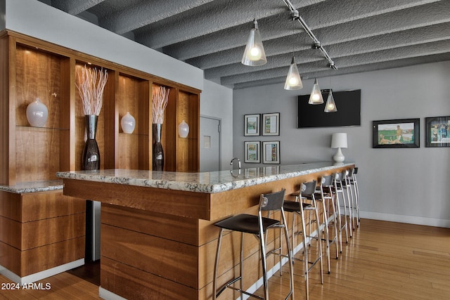 bar with light stone countertops, decorative light fixtures, wood-type flooring, and a textured ceiling