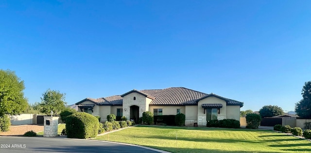 mediterranean / spanish house with stone siding, a tiled roof, a front lawn, and stucco siding