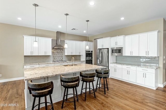 kitchen with stainless steel appliances, a sink, white cabinets, wall chimney exhaust hood, and pendant lighting