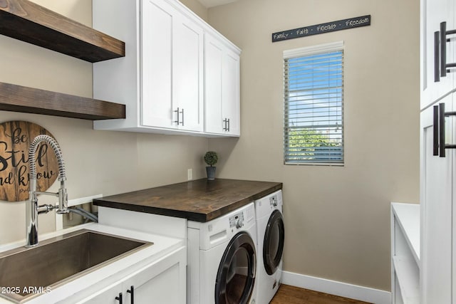 clothes washing area featuring baseboards, a sink, cabinet space, and washer and dryer