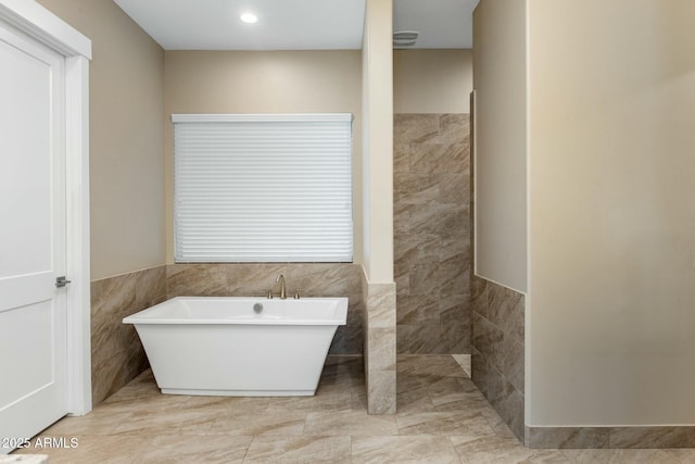 full bath featuring a soaking tub, tile walls, and a wainscoted wall