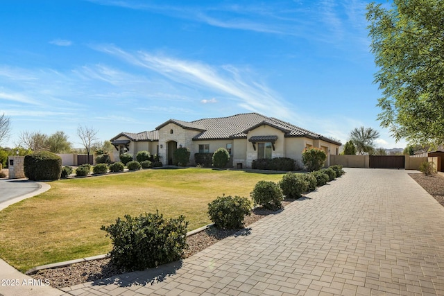 mediterranean / spanish house featuring stone siding, a tile roof, fence, decorative driveway, and a front yard