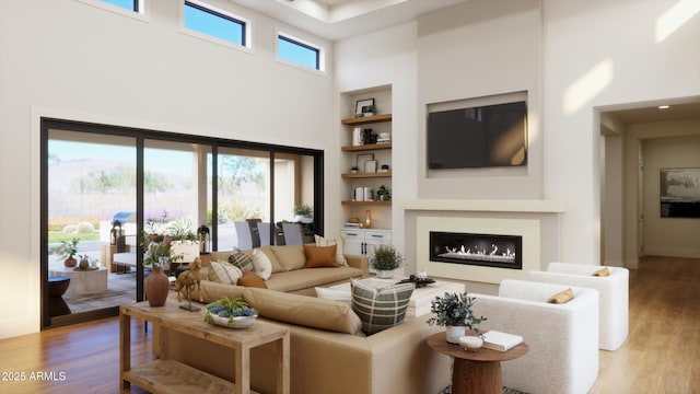 living area featuring built in shelves, a glass covered fireplace, a towering ceiling, and light wood-style floors