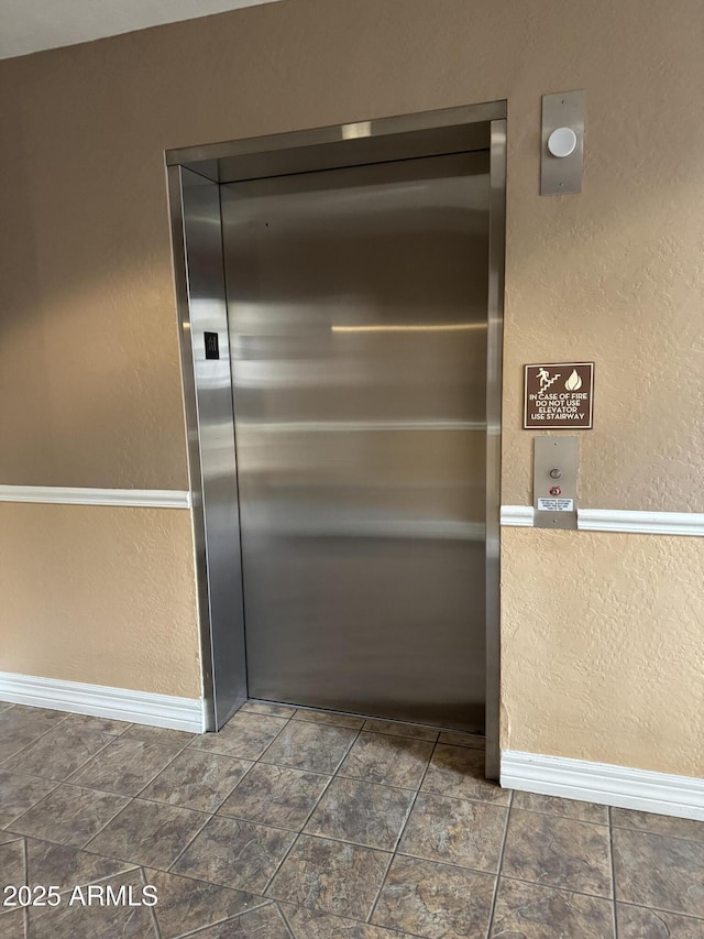 interior details featuring baseboards, a textured wall, and elevator