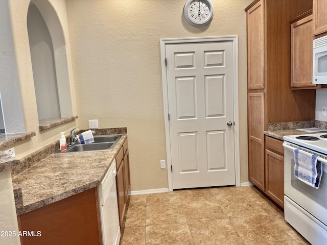 kitchen with white appliances, baseboards, brown cabinetry, a textured wall, and a sink