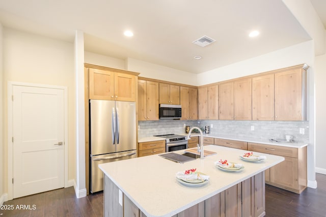 kitchen with tasteful backsplash, appliances with stainless steel finishes, dark wood-type flooring, and an island with sink