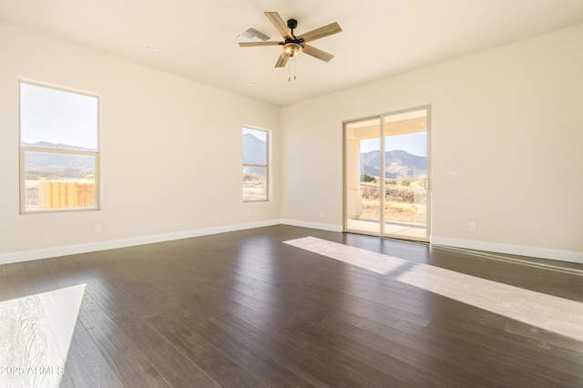 unfurnished room with dark wood-type flooring, ceiling fan, and a mountain view