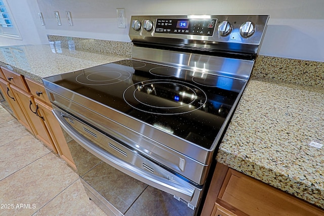 room details with brown cabinetry, stainless steel electric stove, and light stone counters