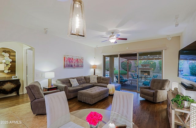 living room featuring arched walkways, wood finished floors, a warm lit fireplace, and a ceiling fan