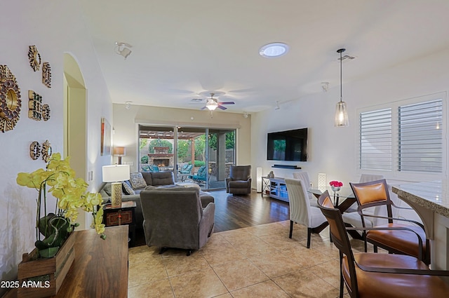 living room with a warm lit fireplace, visible vents, light tile patterned floors, and a ceiling fan