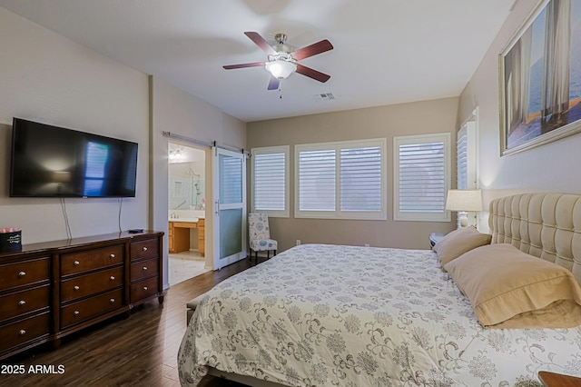 bedroom featuring dark wood finished floors, ensuite bath, a barn door, visible vents, and a ceiling fan