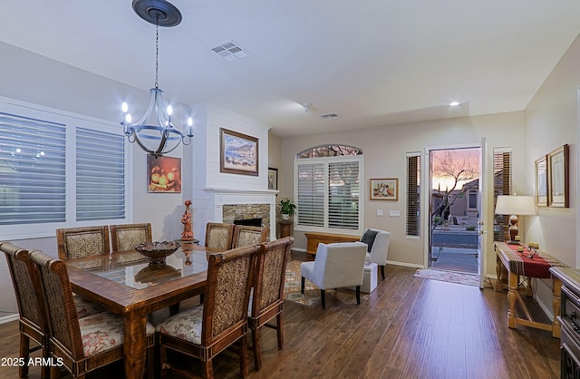 dining area featuring dark wood-style flooring, a stone fireplace, a chandelier, and visible vents