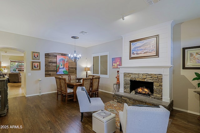 living area with dark wood-style flooring, visible vents, a chandelier, a stone fireplace, and arched walkways