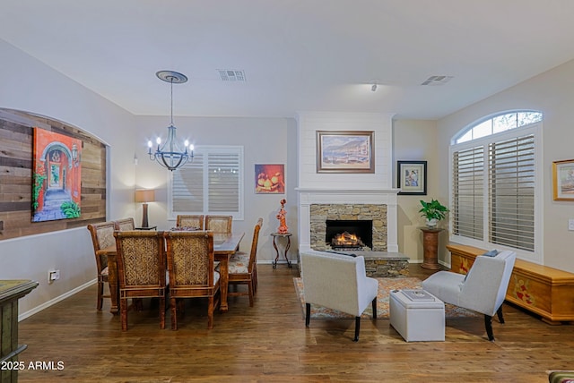 dining area featuring a notable chandelier, wood finished floors, a stone fireplace, baseboards, and visible vents