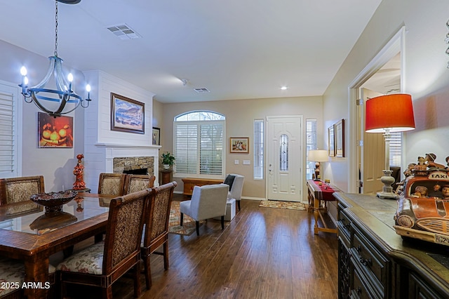 interior space with a notable chandelier, dark wood-style floors, a stone fireplace, and visible vents