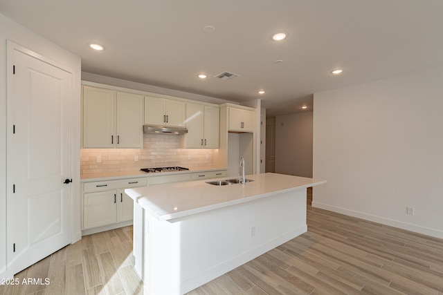 21411 W Meadowbrook Ave, Buckeye, AZ 85396 - kitchen with under cabinet range hood, gas cooktop, tasteful backsplash, light wood finished floors, and light countertops