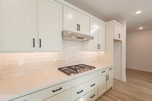 21411 W Meadowbrook Ave, Buckeye, AZ 85396 - kitchen featuring under cabinet range hood, stainless steel gas stovetop, backsplash, white cabinetry, and light wood-style flooring