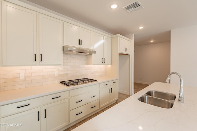 21411 W Meadowbrook Ave, Buckeye, AZ 85396 - kitchen featuring stainless steel gas cooktop, under cabinet range hood, tasteful backsplash, light stone counters, and wood finished floors