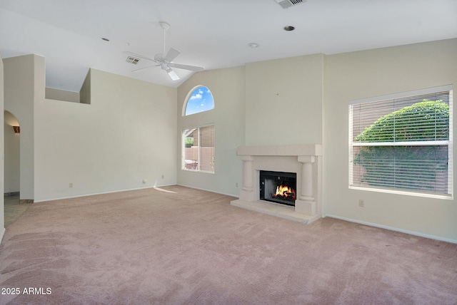 unfurnished living room featuring ceiling fan, light colored carpet, a warm lit fireplace, baseboards, and high vaulted ceiling