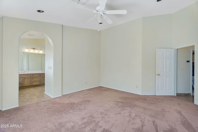 empty room featuring light colored carpet, arched walkways, ceiling fan, a sink, and a towering ceiling