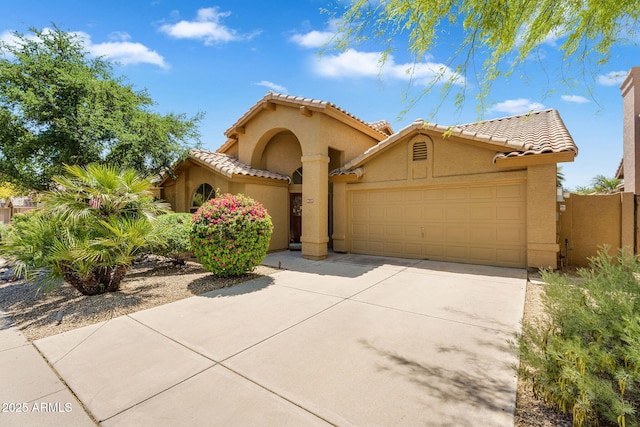 mediterranean / spanish home featuring stucco siding, an attached garage, concrete driveway, a tiled roof, and fence