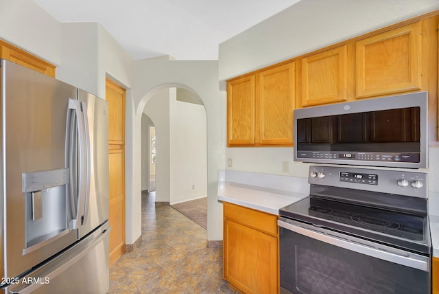 kitchen with appliances with stainless steel finishes, arched walkways, light countertops, and baseboards