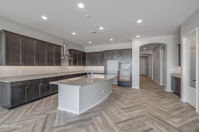 kitchen featuring light stone counters, wall chimney range hood, sink, and light parquet flooring