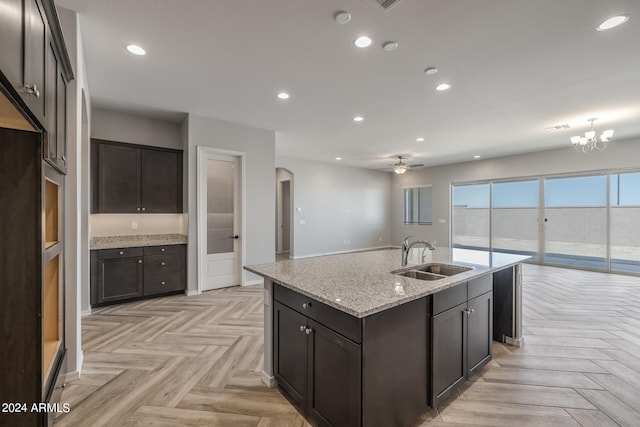 kitchen featuring an island with sink, sink, ceiling fan with notable chandelier, and light parquet flooring