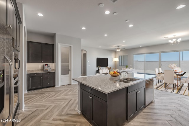 kitchen with stainless steel dishwasher, light parquet floors, light stone counters, sink, and a kitchen island with sink