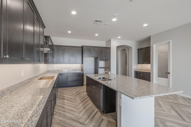 kitchen featuring sink, a kitchen island with sink, light stone countertops, and light parquet flooring