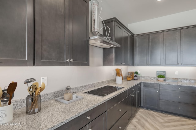 kitchen with light stone counters, light parquet floors, black electric stovetop, wall chimney exhaust hood, and dark brown cabinets