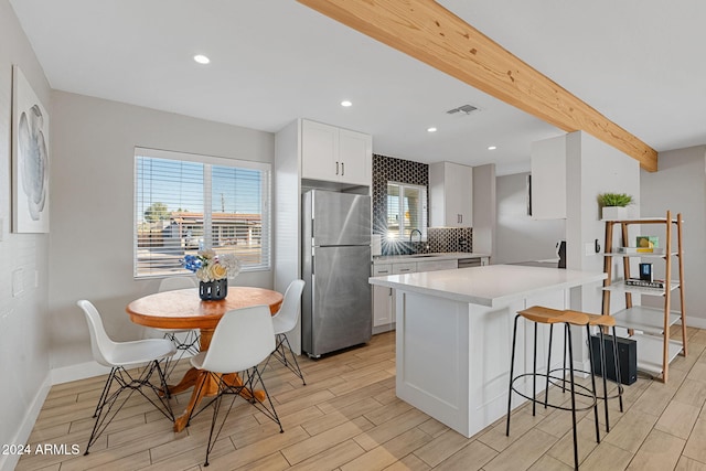 kitchen featuring sink, beam ceiling, white cabinets, light hardwood / wood-style floors, and stainless steel refrigerator