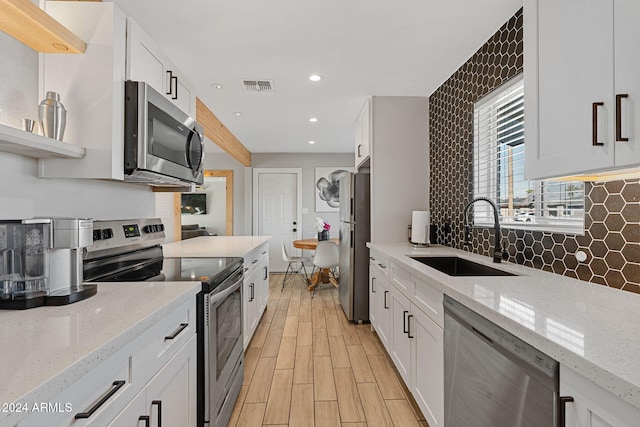 kitchen featuring light stone countertops, appliances with stainless steel finishes, sink, light hardwood / wood-style floors, and white cabinetry