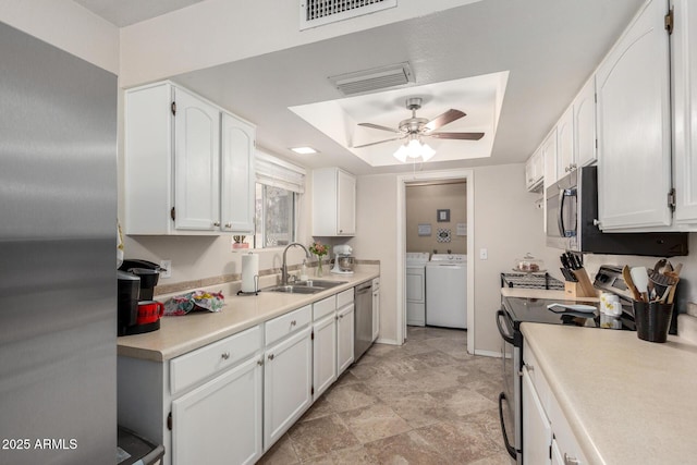 kitchen featuring a tray ceiling, white cabinetry, appliances with stainless steel finishes, and washing machine and clothes dryer