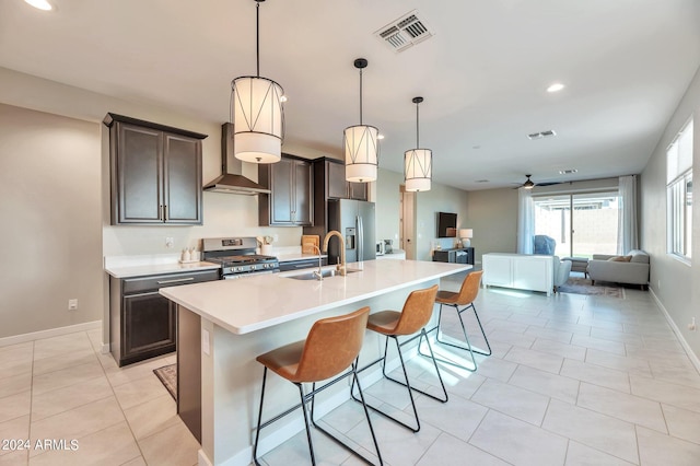 kitchen featuring a kitchen island with sink, a breakfast bar area, sink, wall chimney exhaust hood, and appliances with stainless steel finishes