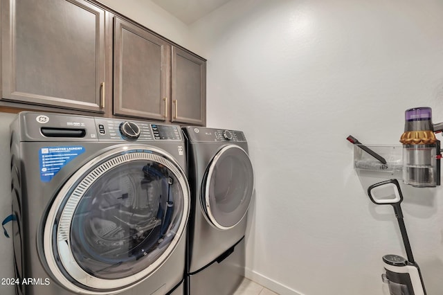 clothes washing area with washing machine and dryer, light tile patterned flooring, and cabinets