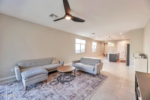 tiled living room featuring ceiling fan with notable chandelier and sink