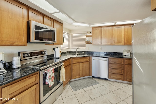 kitchen with dark stone counters, appliances with stainless steel finishes, light tile patterned floors, and sink