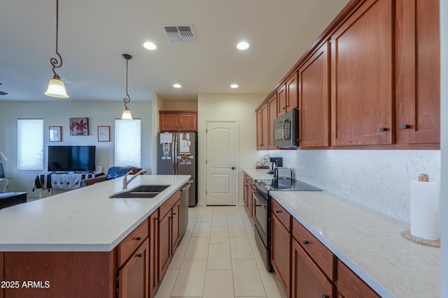 kitchen with sink, hanging light fixtures, stainless steel appliances, light stone countertops, and a center island with sink