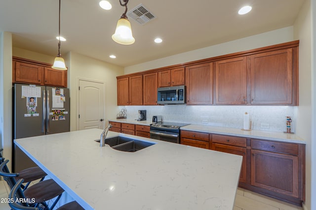 kitchen with sink, a kitchen island with sink, backsplash, stainless steel appliances, and decorative light fixtures