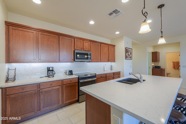 kitchen with hanging light fixtures, appliances with stainless steel finishes, a kitchen island with sink, and sink