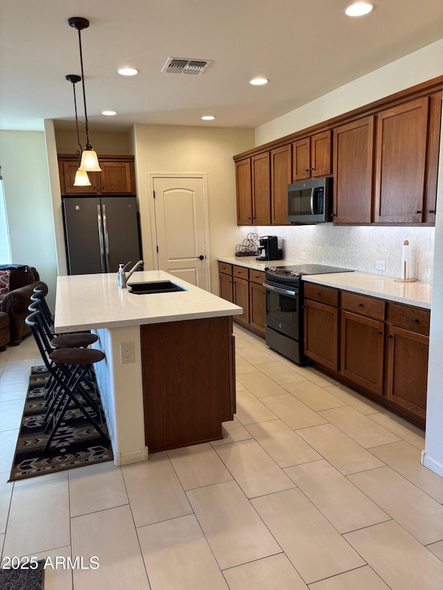 kitchen with sink, a kitchen island with sink, hanging light fixtures, stainless steel appliances, and tasteful backsplash