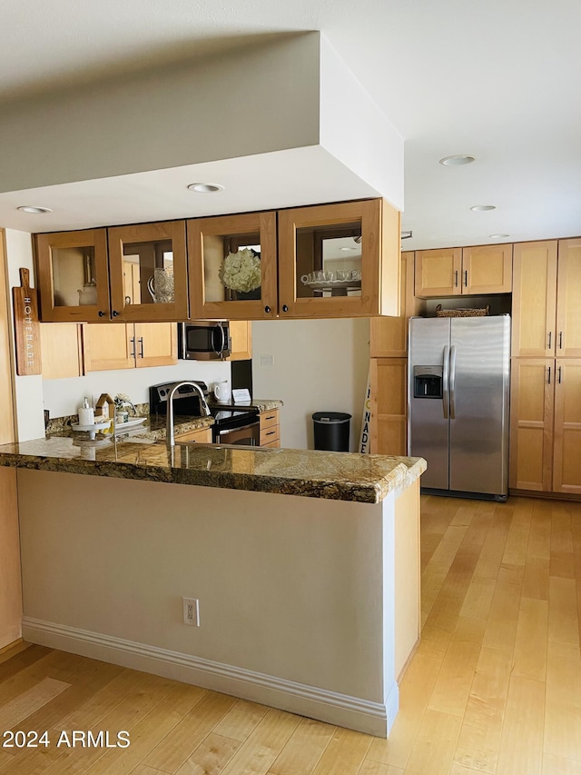 kitchen featuring a peninsula, appliances with stainless steel finishes, dark stone countertops, and glass insert cabinets