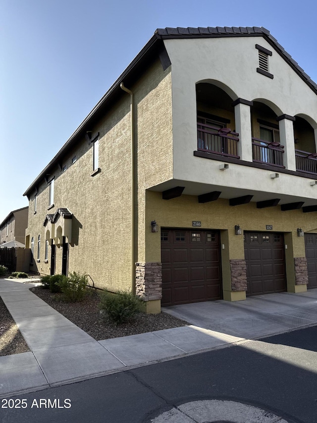 2725 E Mine Creek Rd Unit 2146, Phoenix, AZ 85024 - view of front of property featuring stucco siding, a balcony, driveway, an attached garage, and stone siding
