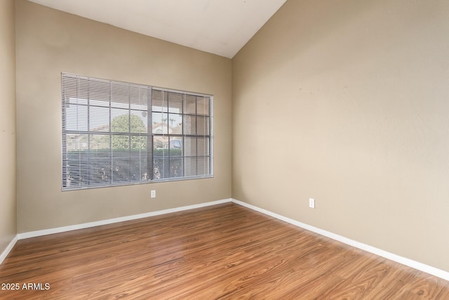 empty room with lofted ceiling, wood finished floors, and baseboards